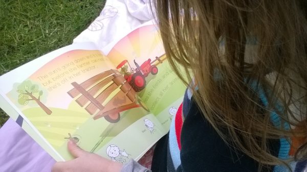 Image shows a young female child reading an award winning colourful farm themed picture story book with sign language to support the storyline